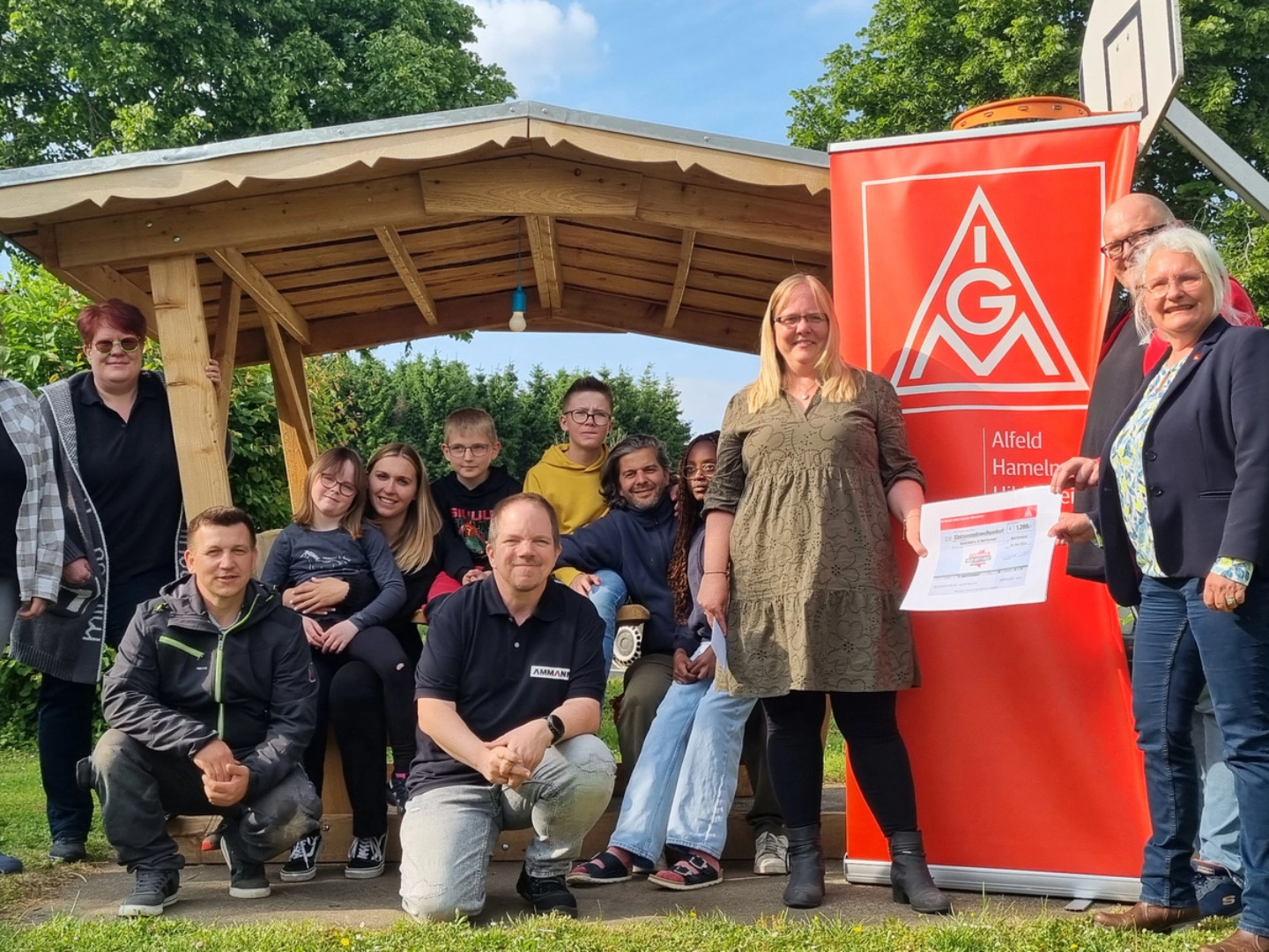 Thomas Ergezinger, Phoenix Contact (2.v.re.) und Karoline Kleinschmidt (re.) überreichen Katrin Tutsch-Watermann (3. v. re.) gemeinsam mit Marcus Van Son, Ammann ABG (kniend, Bildmitte) und Iris Ergezinger, Phoenix Contact (2. V. li.) im Beisein der Kinder und Jugendlichen sowie den Mitarbeitern des Kunterbunt e. V. den symbolischen Spendenscheck.