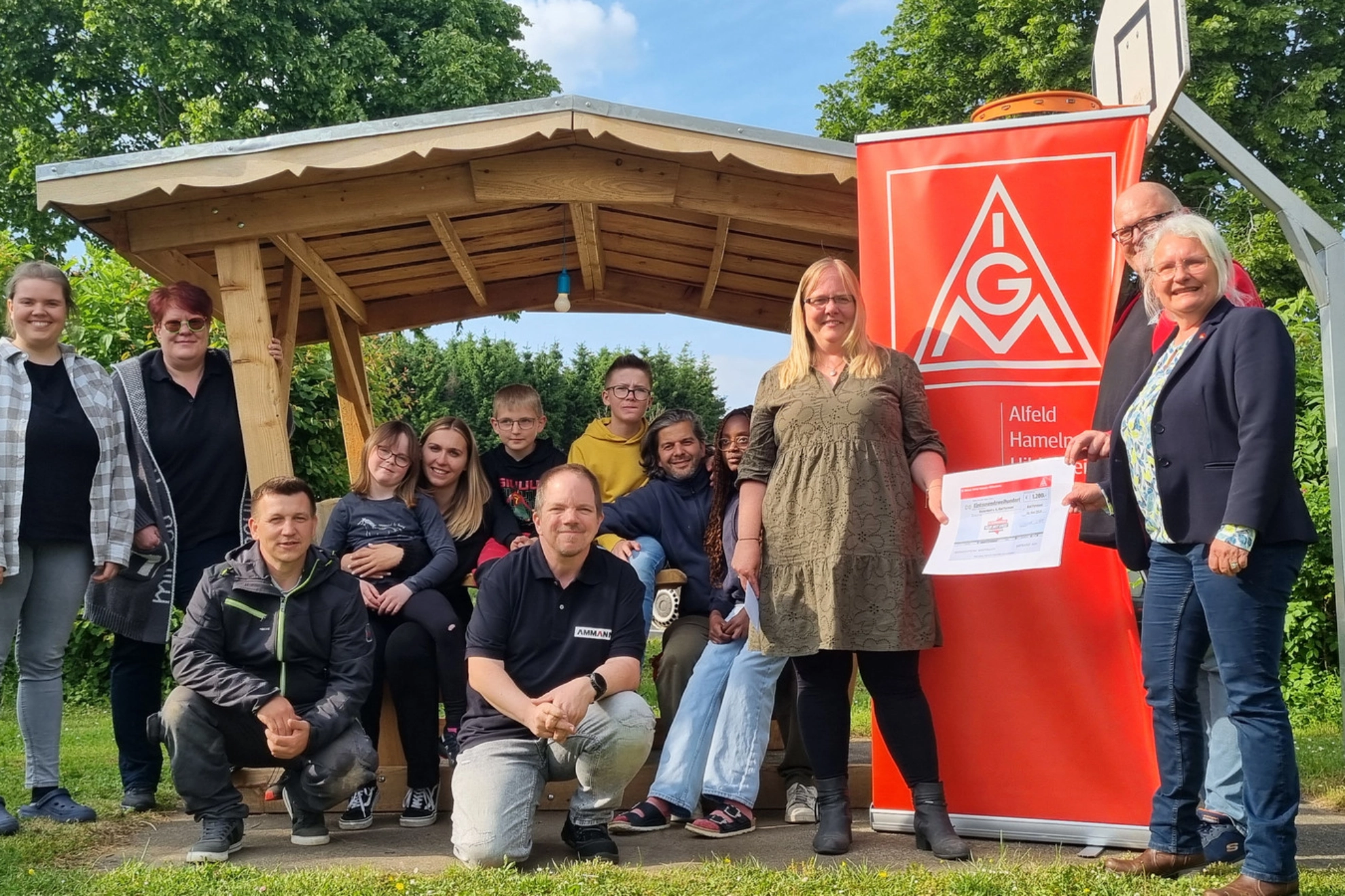 Thomas Ergezinger, Phoenix Contact (2.v.re.) und Karoline Kleinschmidt (re.) überreichen Katrin Tutsch-Watermann (3. v. re.) gemeinsam mit Marcus Van Son, Ammann ABG (kniend, Bildmitte) und Iris Ergezinger, Phoenix Contact (2. V. li.) im Beisein der Kinder und Jugendlichen sowie den Mitarbeitern des Kunterbunt e. V. den symbolischen Spendenscheck.